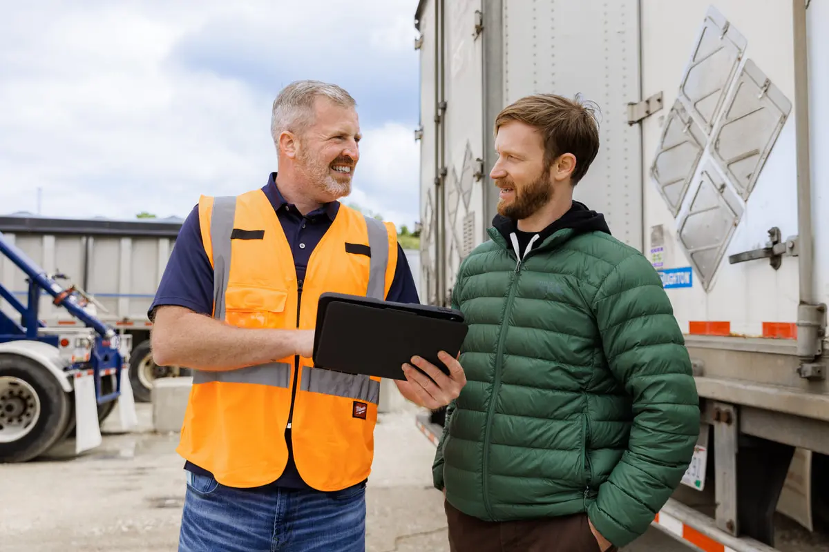 A man in a hi-vis vest going over a tablet with a driver beside a trailer